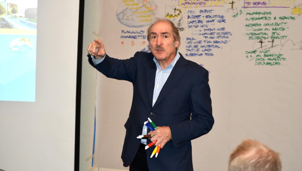 man pointing with white board behind him