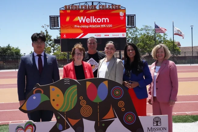 trustees pose in front of stadium scoreboard showing "Welkom"